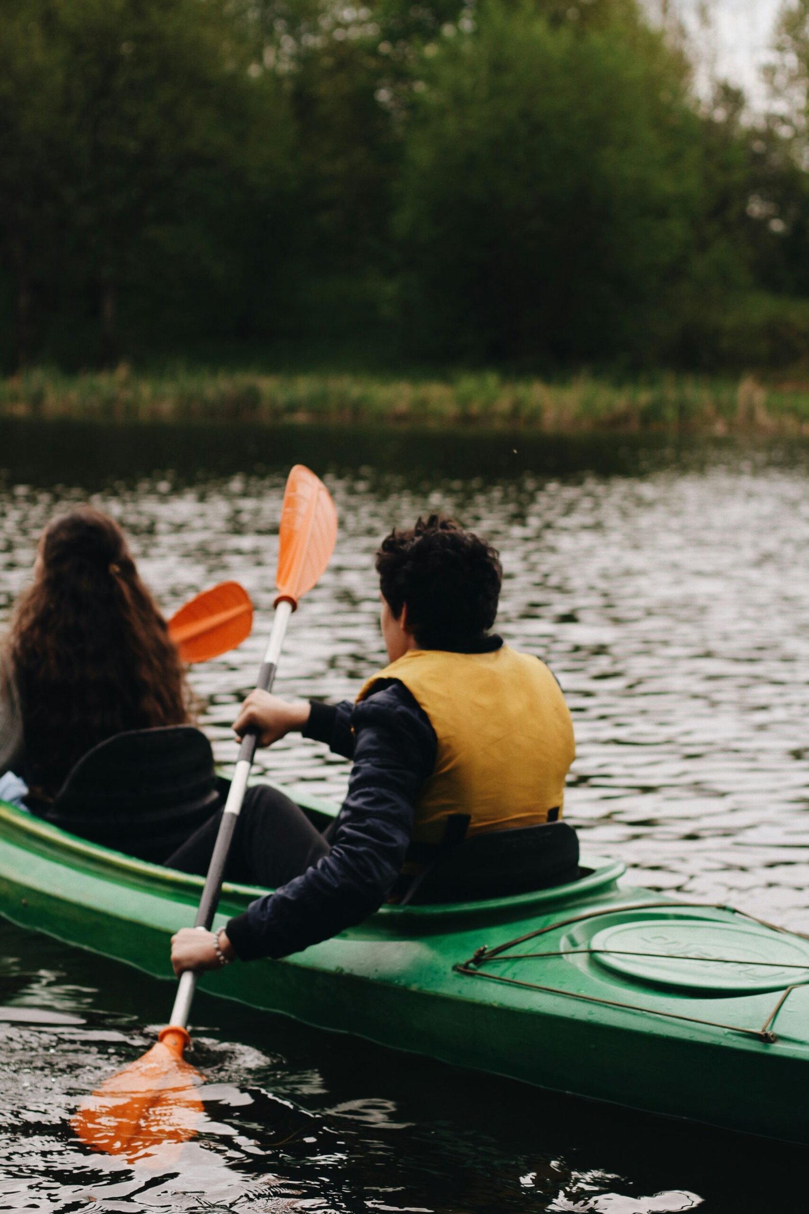 woman in yellow and black jacket riding green kayak on lake during daytime